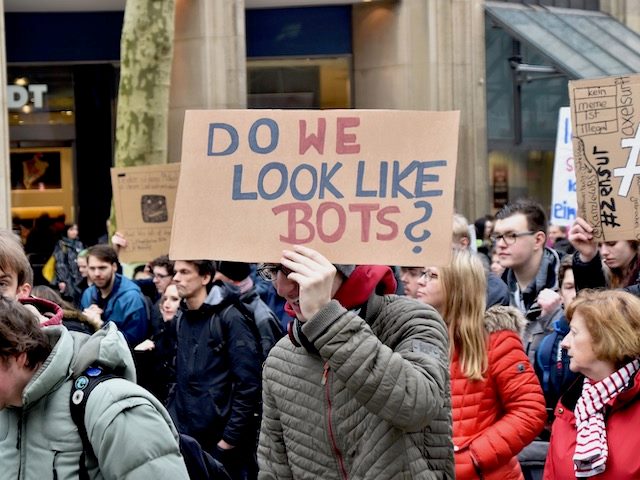 people at a rally holding a sign reading "do we look like bots?"