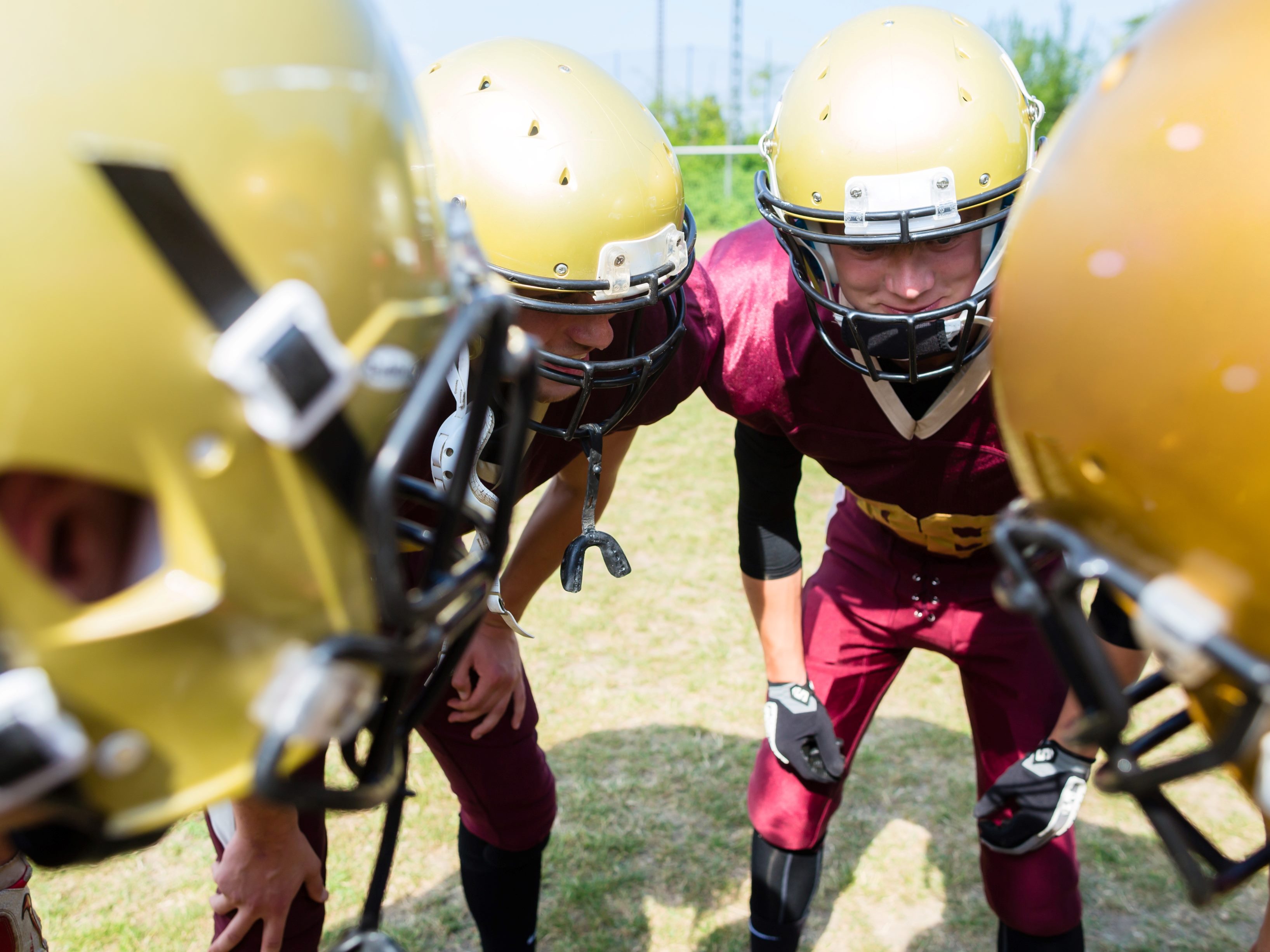 Young American football players wearing red uniforms and yellow helmets gather in a strategy huddle, suggesting the importance of AI strategy.