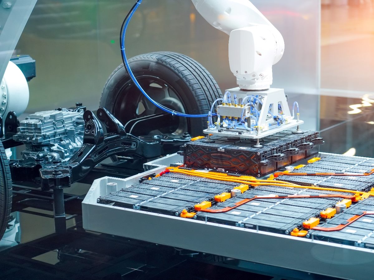 Robotic arm assembling or inspecting the battery pack of an electric vehicle chassis, showcasing components such as the battery modules, wiring, and drivetrain.
