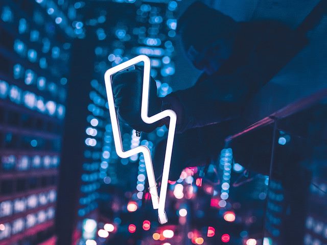 a person holding a neon lit lightning bolt  over chicago cityscape