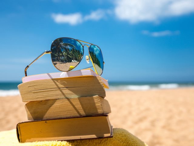 a pair of aviator sunglasses on top of a stack of books on the beach