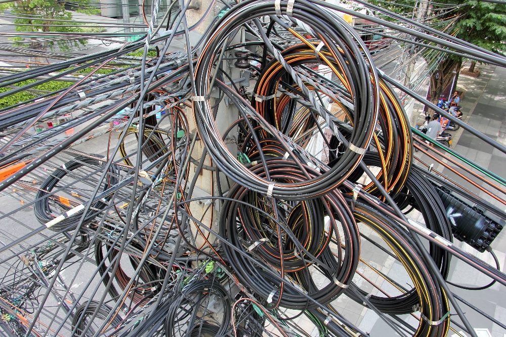 Tangles of chaotically messy of electric cable in grays, reds, yellows and blacks in rolls and unspooled, suggesting the complications that can come from new technology adoption.