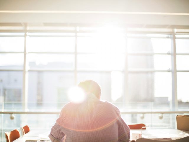 An employee reads in an office conference room with bright sunlight.