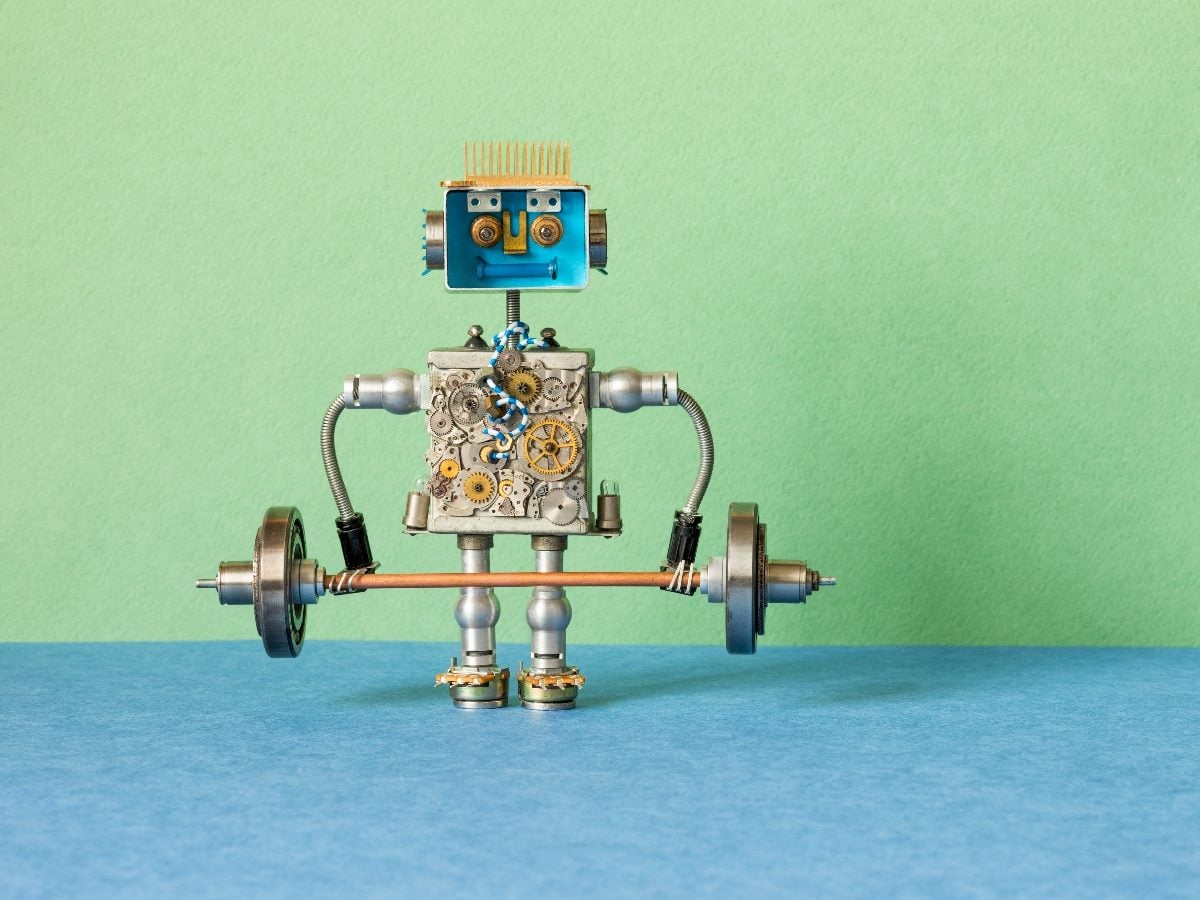 A small toy robot made from metal parts and gears stands upright while lifting a miniature barbell, set against a green and blue background.