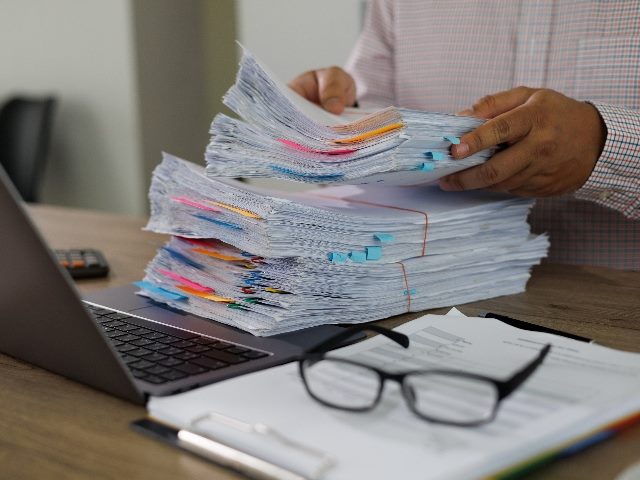 Data documents on office desk, in front of a laptop, as a pair of hands holds the paper stack.