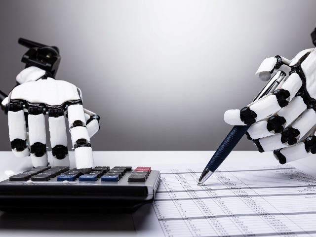 White robot hands with black accents examines financial papers and pecks at a calculator and takes notes with a black pen. 