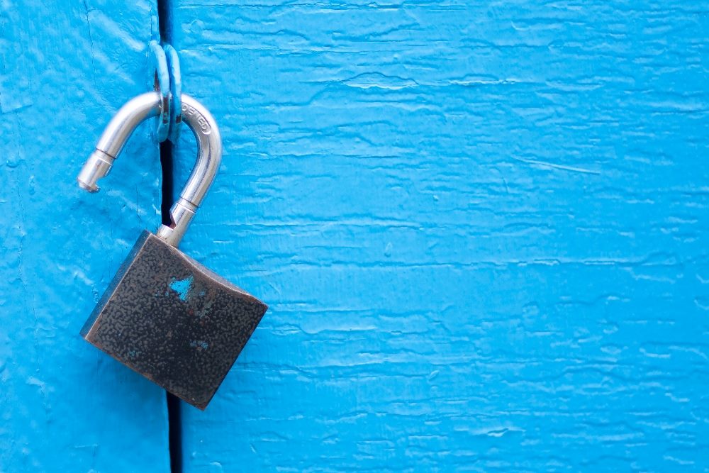 An open metal padlock hangs from a bright blue metal door, suggesting the potential opportunities Net Promoter Score can unlock.