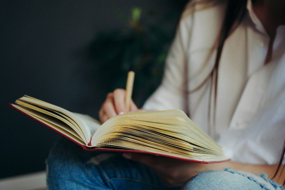 A person sits holding a journal on their knee while writing with a pen in piece about AI in analytics and workflow tips.