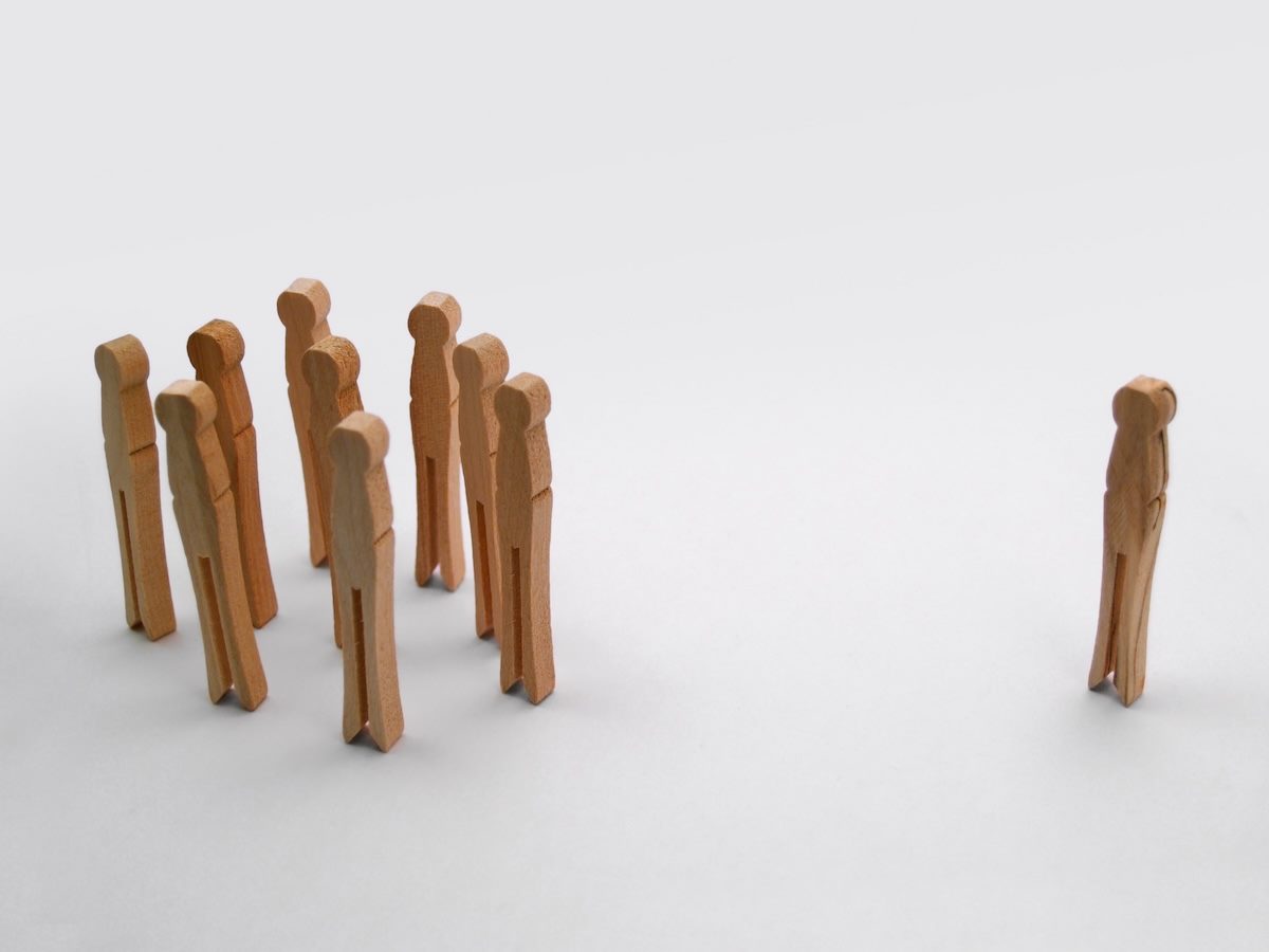 a group of clothespins standing up, looking kind of like people, with an odd one off to the side, outside of the group