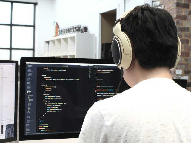 A software engineer with headphones writes code on a computer at an office desk.