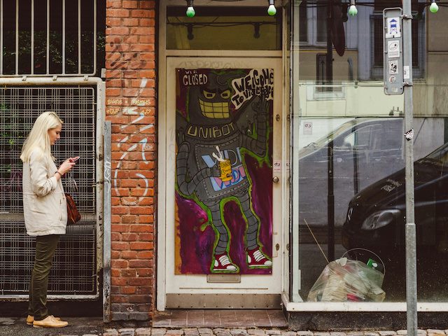 woman searching on smartphone next to robot graffiti