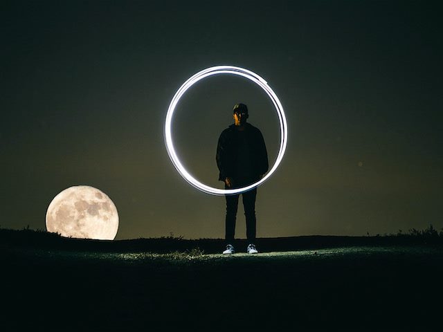 holding a lit circle with a full moon behind