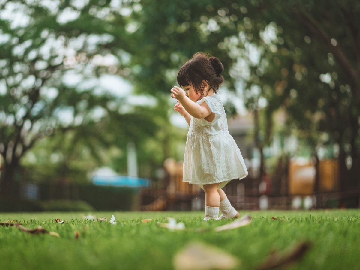 Baby taking steps on green grass in park.