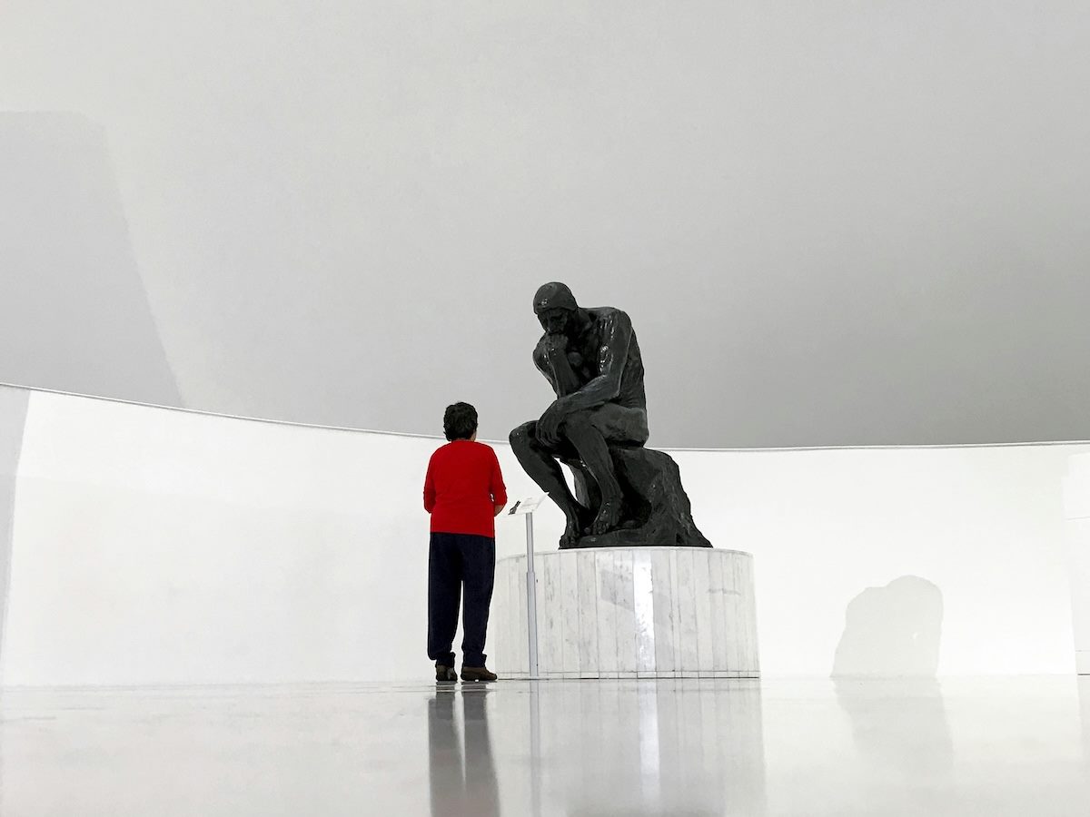 a person standing in front of the sculpture "The Thinker," thinking