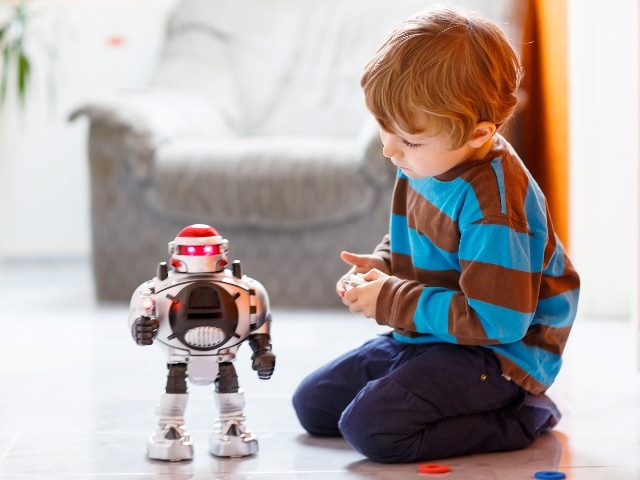 A child wearing a blue and brown striped shirt and jeans plays with a red and white toy robot on a living room floor with a chair in the background, indicating the need for trust when using  AI  in digital marketing. 