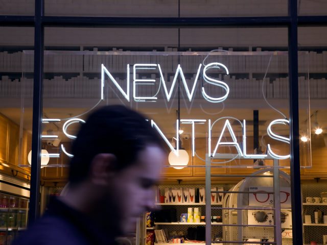 man walking by a window with a neon news essentials sign