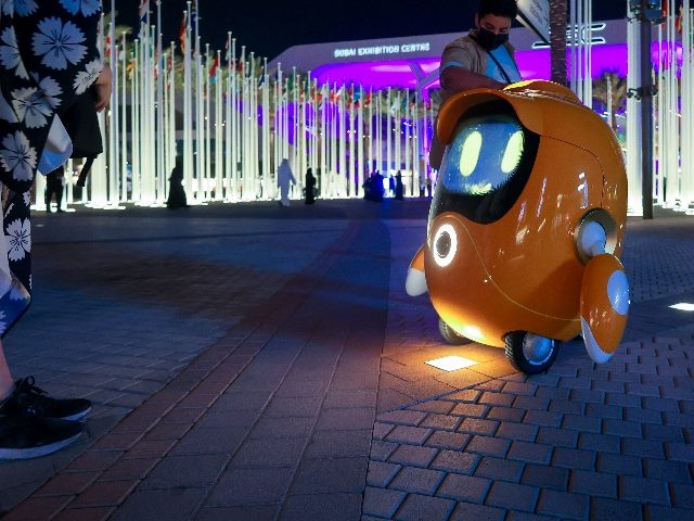 Small robot mascot looks toward a human.