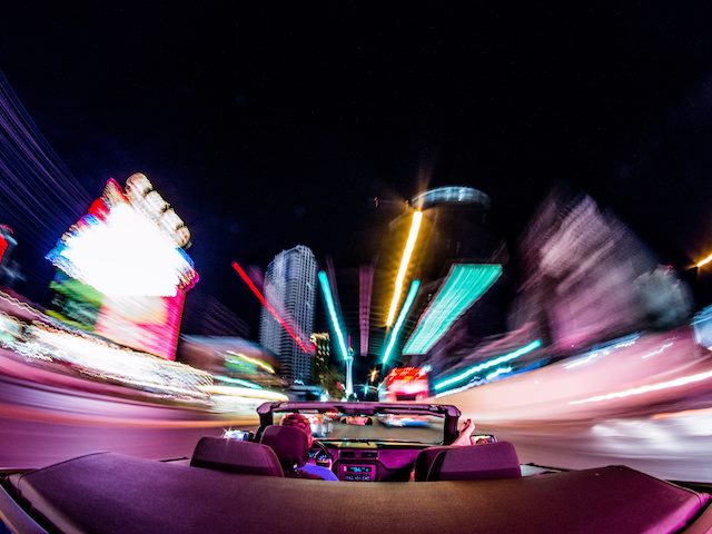 convertible accelerating past neon signs