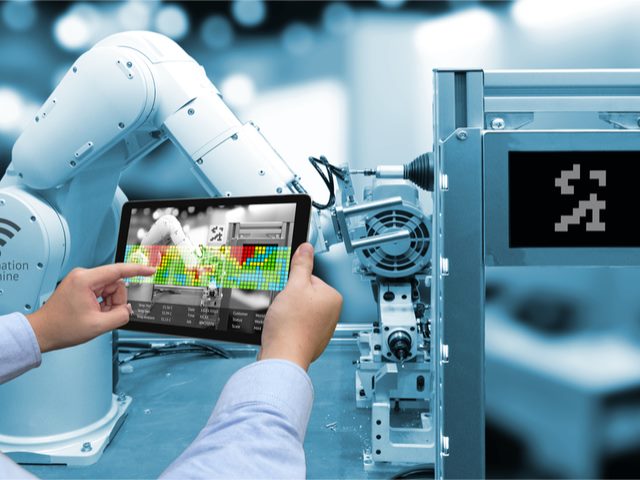 Man hand holding tablet with Augmented reality screen software and blue tone of automate wireless Robot arm in smart factory background