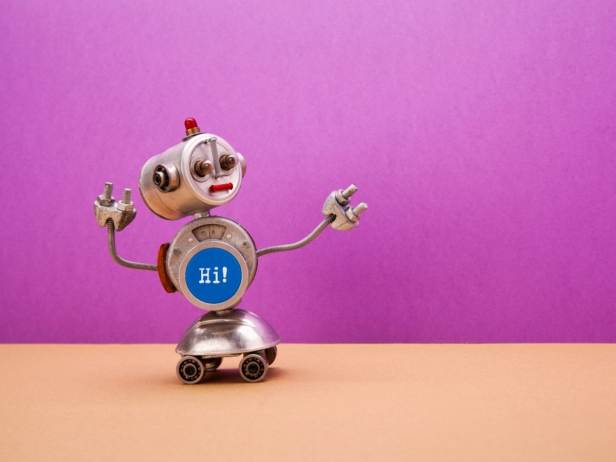Toy robot with a round body and wheels, holding its arms up and displaying a blue circle on its chest with the word “Hi!” against a purple background.