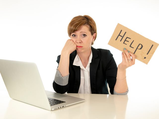 A CIO at her desk with a laptop on it. The woman looks upset and is holding a sign that says "help."