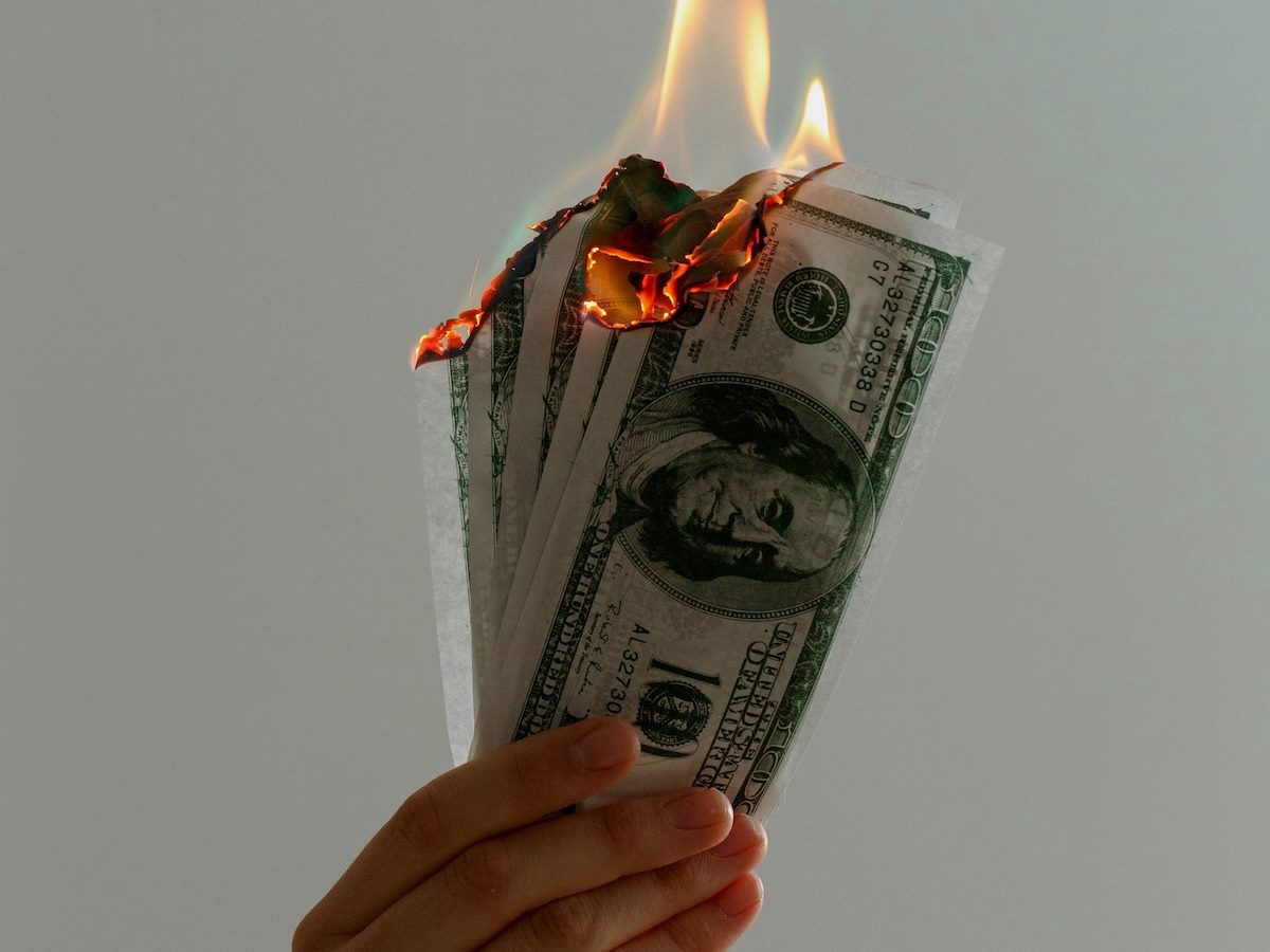 a close up of a hand holding a number of $100 bills on fire 