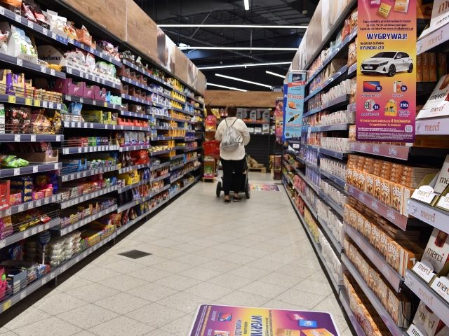 Scene of grocery-shopping aisle with shopper pushing carriage in the distance. 