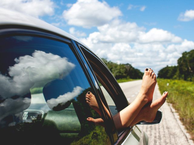 A passenger hangs their feet out of a car window.