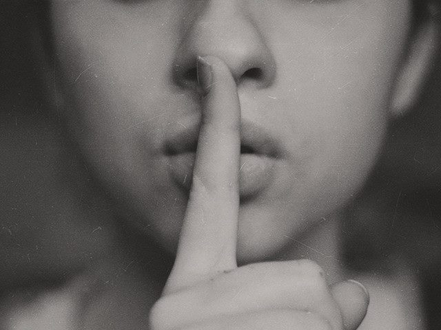 close up of woman holding finger before her lips "shhhhhhhhh"