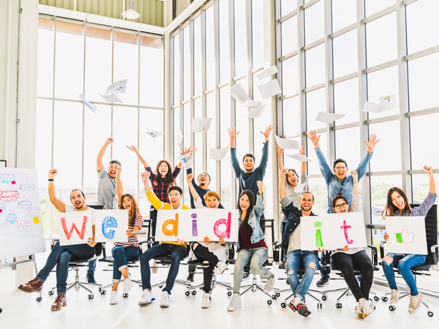 Happy business people in their office, cheering together, celebrating their project success