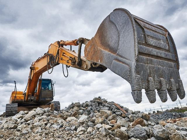A bright yellow excavator loader machine digs into the rocks at a demolition construction site, suggesting the need for effective CX strategies. 