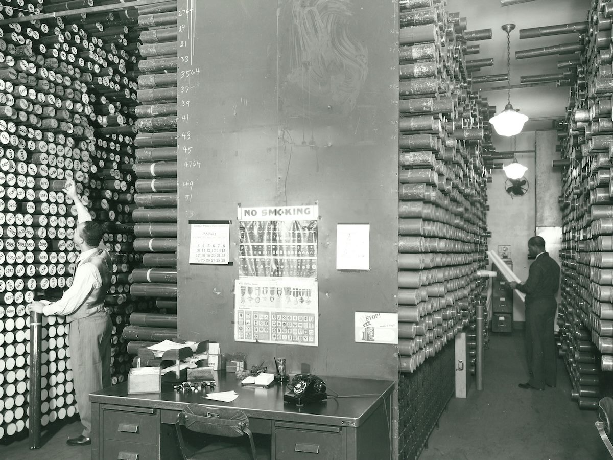 black and white photo of an old NOAA office with an inventory of hydrographic surveys lining the walls in cardboard tubes