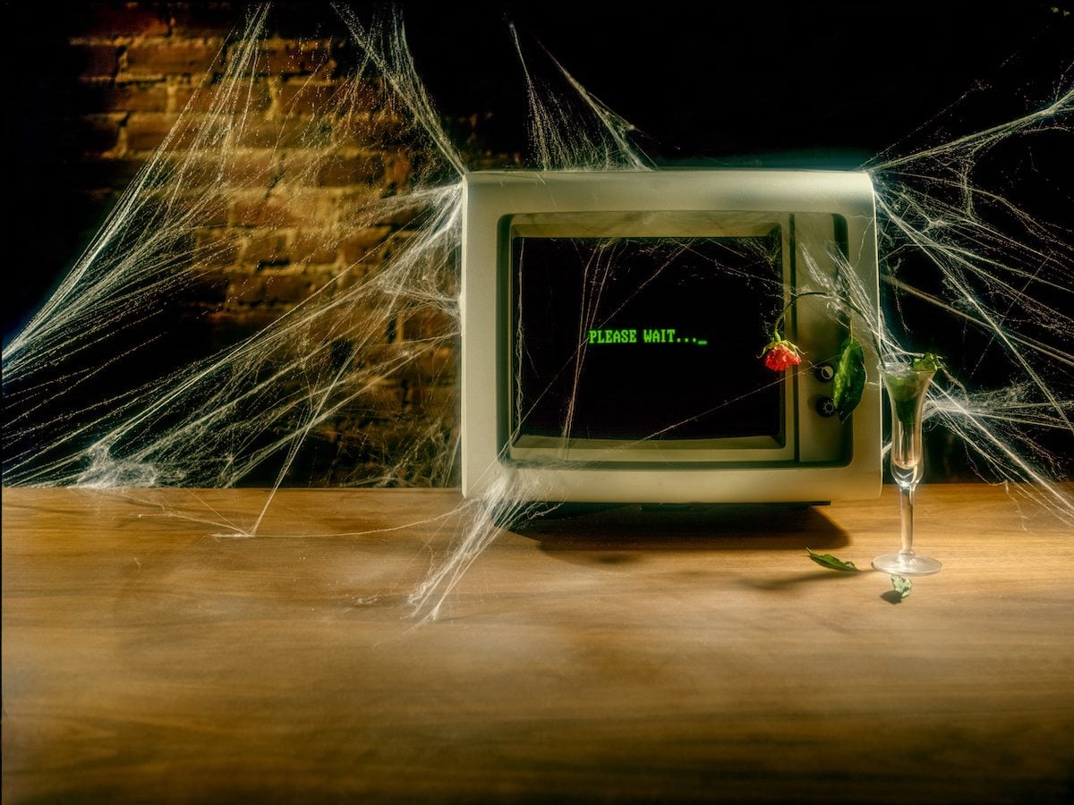 old computer on desk with cobwebs and "please wait" on screen 