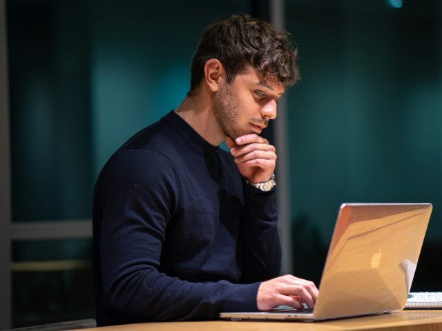 An employee stops to think while working on a laptop computer.