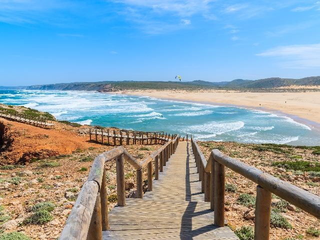 Wooden walkway at Bordeira beach down toward blue ocean view, in the Algarve region, Portugal. 