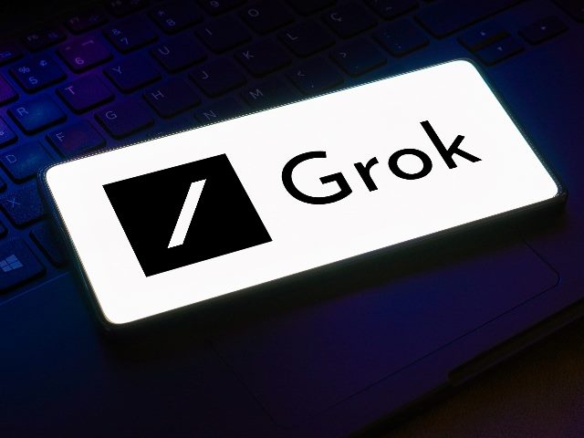 The Grok logo on a smartphone superimposed on a dark blue-lit background on a keyboard, in piece about the launch of Elon Musk's new conversational AI tool, Grok. 