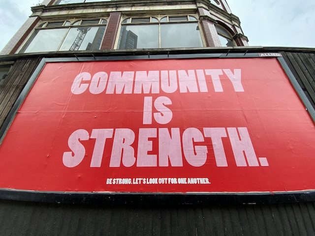 A Billboard that reads "Community Is Strength" with the subtext: "be strong. let's look out for one another"