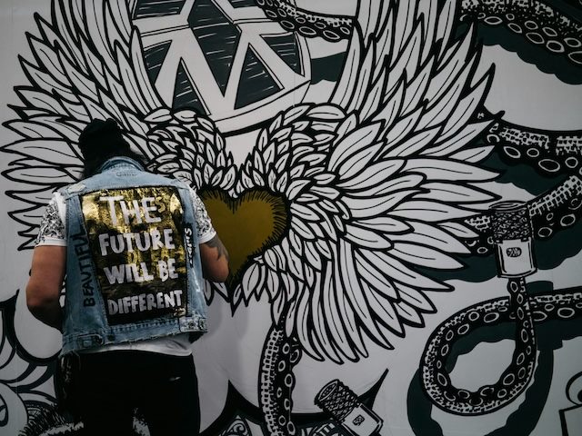 artist painting a mural on a wall. the artist is wearing a vest with the words "the future will be different"