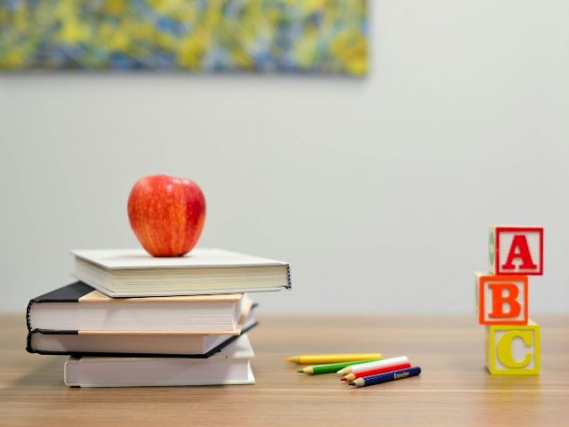 Books, an apple, pencils, pens and letter blocks on a desk.