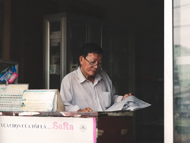 man working in newsstand reading a paper