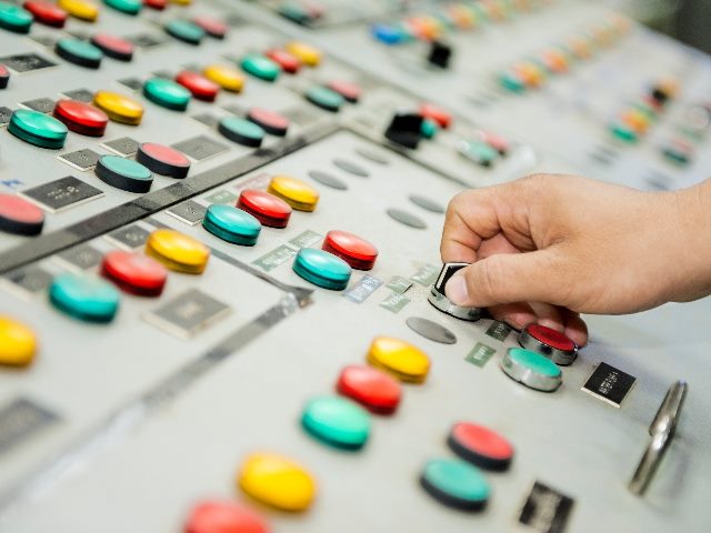 A man's hand twists a metal know on a control panel of blue green, yellow and blue buttons, suggesting the need for leaders to enable AI in customer experience.