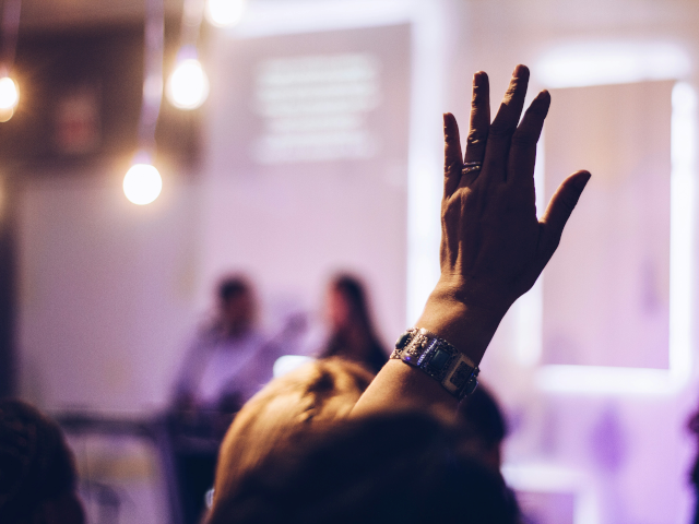 An attendee raises their hand to ask a question at a business event.