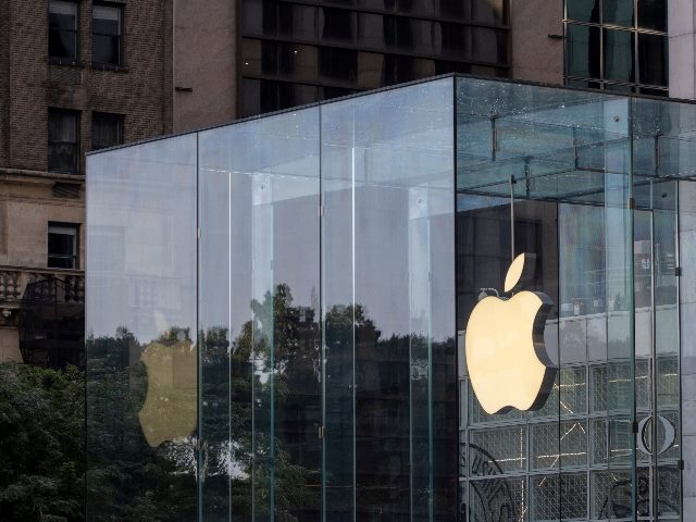 This image shows the exterior of an Apple Store, notable for its modern design featuring clear glass walls and a large, luminous Apple logo affixed to the glass. The surroundings reflect urban elements, including neighboring buildings and a glimpse of greenery, possibly from trees or a park nearby. The photograph captures a mix of technology and urban environment, highlighting Apple's iconic branding and architectural style in piece about Apple's AI rollout at WWDC 2024. This is the Apple flagship store on the 5th Avenue in NYC.