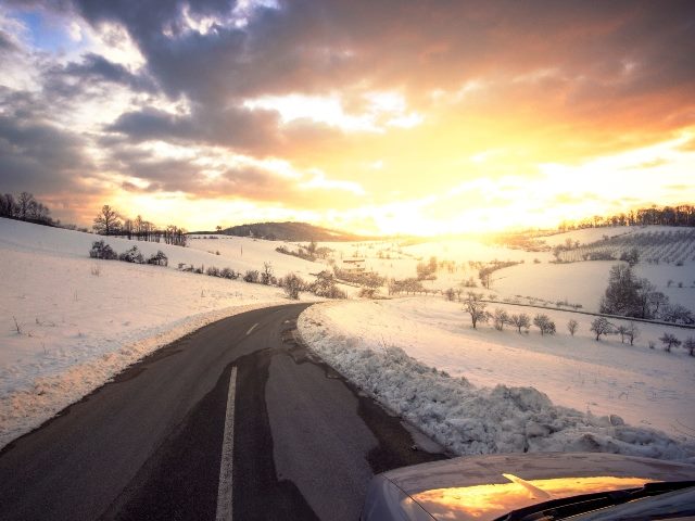 Beautiful sunset in January with a road ahead, surrounded by snow. 