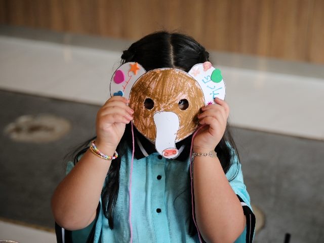 Little child wearing a colored animal paper mask fronting her face, representing the rising issue of deepfakes online. 