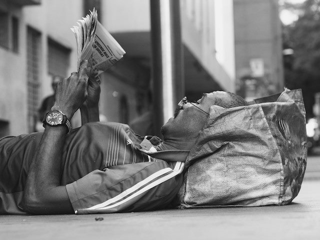 laying on the sidewalk, reading a newspaper