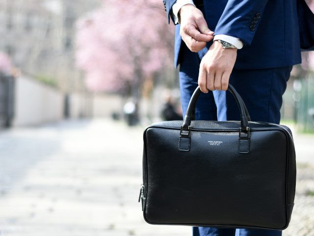 A person holds a briefcase on a sidewalk.