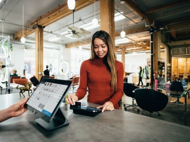 Woman swiping a credit card and at a store's check-out counter.