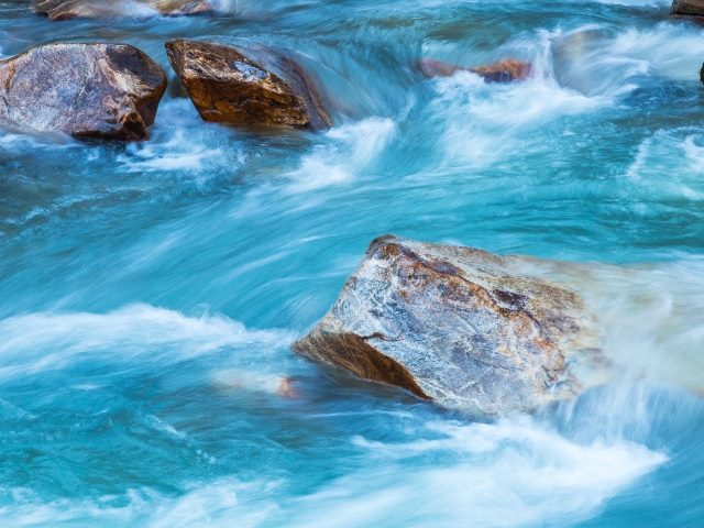 Aqua colored glacier-fed river water churns among rocks. 