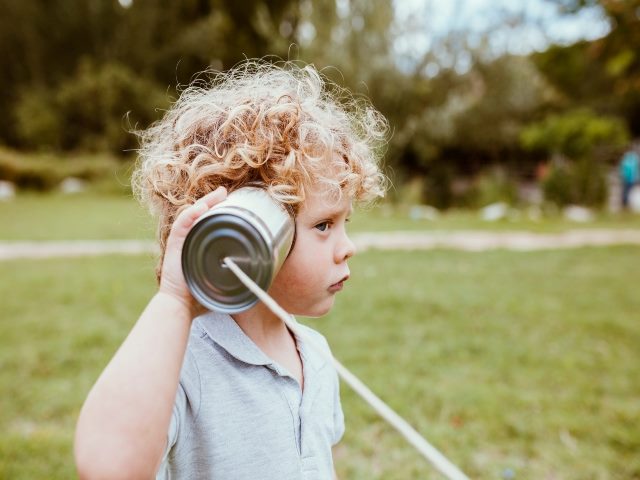 Child holds a can attached to a string up to his ear and listens
